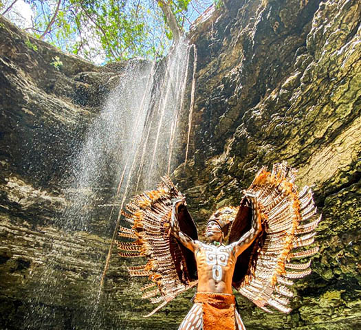 guerrero maya con traje de buho abre las alas en la cascada del cenote chichikan eco parque en valladolid yucatan